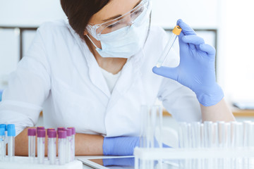 Close-up of professional female scientist in protective eyeglasses making experiment with reagents in laboratory. Medicine and research concept