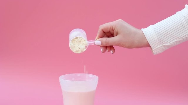 Female hand pours shaker protein on pink background, copy space.