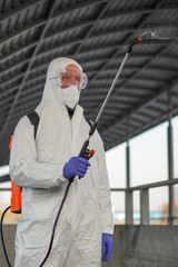 A man in protective equipment disinfects with a sprayer in the city. Surface treatment due to...