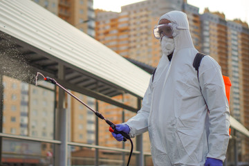 A man in protective equipment disinfects with a sprayer in the city. Surface treatment due to...