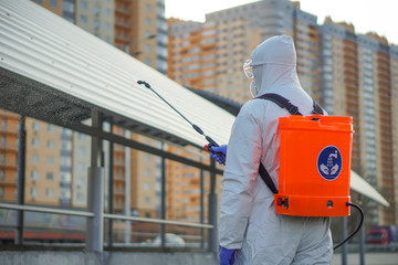 A man in protective equipment disinfects with a sprayer in the city. Surface treatment due to...