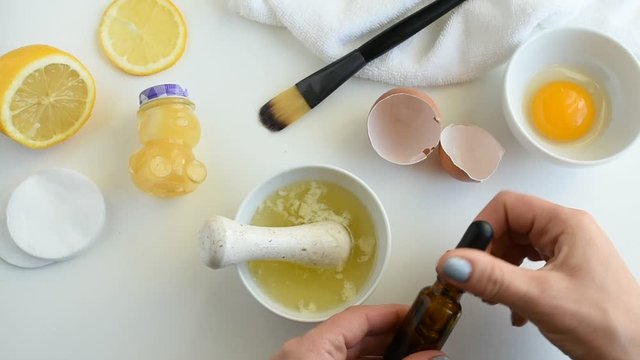 Woman mix facial mask for acne treatment from honey, egg white, lemon and tea tree oil. Natural homemade cosmetics.