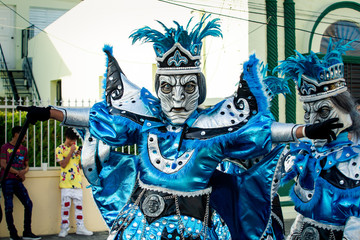 man in variegated blue costume poses for photo on city street at dominican carnival - obrazy, fototapety, plakaty