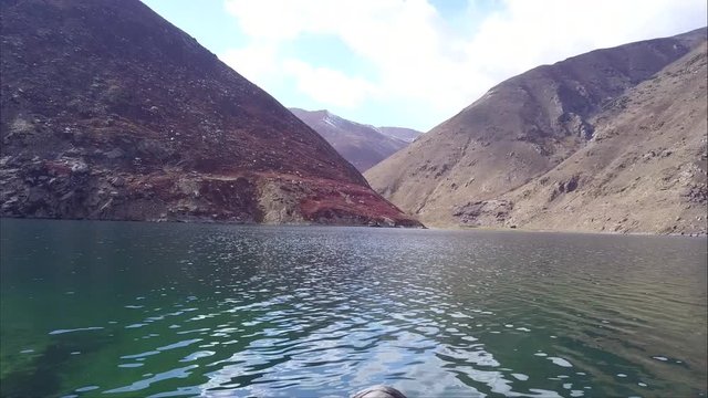 A traveler sitting at the bank of crystal clear water of Lulusar lake showing his trekking boots and enjoying the views of Pakistan northern areas mountains whose colors are brown in autumn