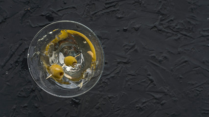Dirty martini with green olive in a cocktail glass on black concrete