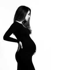 Fototapeta premium Black and white photo of pregnant female in tight dress. She put hands on her belly, posing isolated on white background. Close up