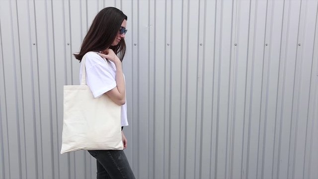 Young woman holding white textile eco bag againstwhite wall. Ecology or environment protection concept. White eco bag for mock up.