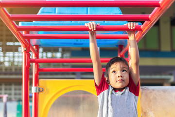 Kid exercise for health and sport concept. Happy Asian student​ child boy playing and hanging from a steel bar at the playground. 5-6 years old.