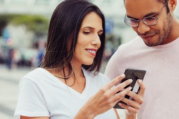 Front view of good friends looking at smartphone. Smiling multiracial colleagues looking at phone on street. Communication and technology concept
