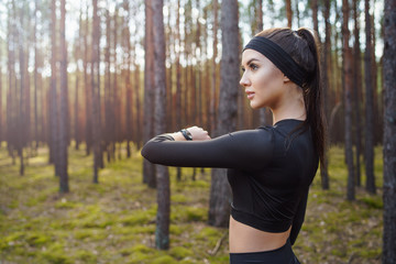 Woman running in the woods checking smartwatch. Natural light in forest. 