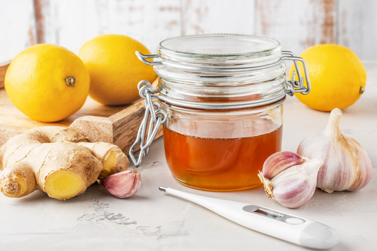 Alternative medicine, natural home remedy for cold and flu. Glass jar with honey, lemon, ginger, garlic and thermometer