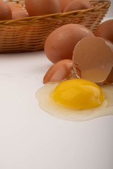 A broken chicken egg, chicken eggs in a wicker basket and chicken eggs scattered on a white background. Close up.