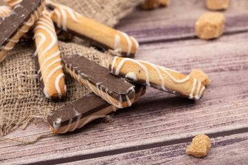 Cookie sticks with white icing and chocolate and pieces of brown cane sugar on a wooden background. Close up.