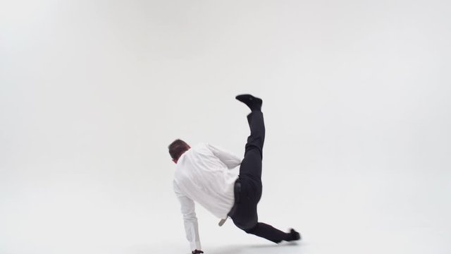 A guy in office clothes turns on his hands and stands up. Office clerk dancing bottom break on a white background. Businessman dancing breakdance and spinning on his hands