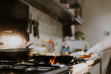 Chef in restaurant kitchen at stove with pan, doing flambe on food