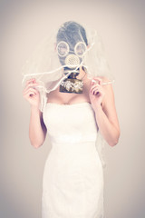 Bride in veil dress and protective mask in a gas mask posing on a delicate background