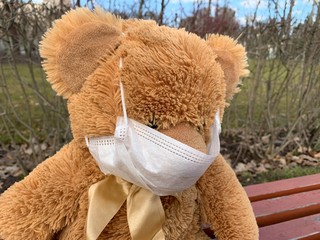 Lonely Teddy Bear in the medical mask on a bench