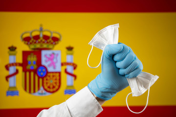 Hand with a glove holding a mask and the Spanish flag in the background coronavirus
