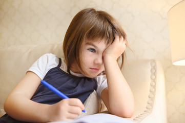 little girl child 7 years old schoolgirl sitting at home on the sofa with a notebook doing homework lessons
