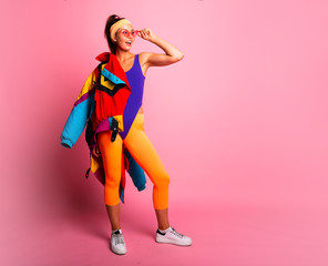 Full length fashion portrait of young trendy woman in cap and jeans looking away.young and cool, hipster girl with colored coat, orange leggings  and body suit. 80s 90s style