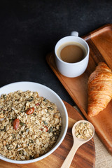 Granola bowl, coffee and croissant on black background. Top view. Copy space.
