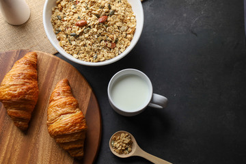 Granola bowl, croissant and milk on black background. Top view. Copy space.