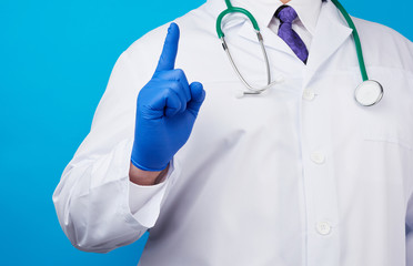 male doctor in white coat, blue medical gloves shows hand gesture of attention