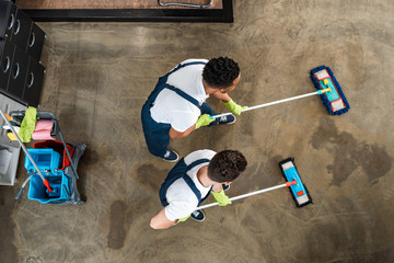 top view of two multicultural cleaners washing floor with mops