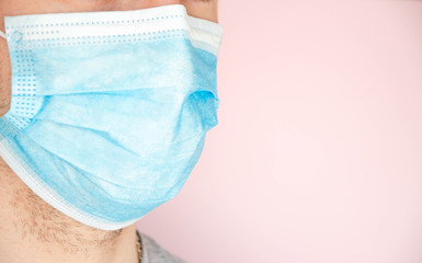 A man in a blue medical mask looks at the camera, sideways. A man in a gray T-shirt on a pink background. Place for text. Copy Space.  COVID-19