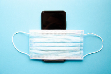 Blue medical mask on a black smartphone. Protection, disinfection of the smartphone. The mask is dressed on a smartphone on a blue, black, pink, yellow background.  Copy Space.  COVID-19