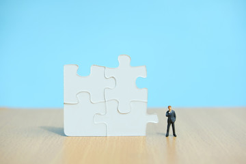 Conceptual photo of business strategy – miniature people standing in front of four joined jigsaw puzzle