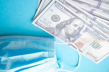 Blue medical mask with dollars on a blue, yellow, pink background. Mask and 100 dollar bills on a black background.  Copy Space.  COVID-19