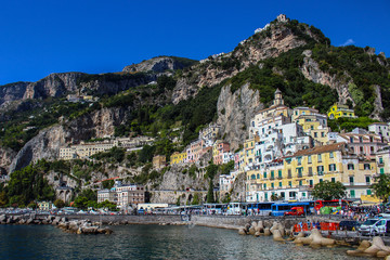 Fototapeta na wymiar View of the city of Amalfi from the jetty with parked buses, the sea and the colorful houses on the slopes of the Amalfi coast in the province of Salerno, Campania, Italy.