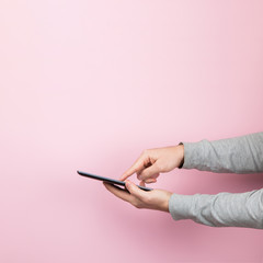 The man's hand holds the smartphone on pink background, concept. Tochscren tablet, copy space.