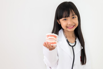 Asian child girl dressed in a doctor's outfit in her hand holding a dental model with a smiling face on a white background.