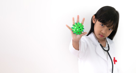 Asian child girl in a white doctor's outfit is raising his hand to protect against a green, spiky green toy, the idea of a dangerous virus prevention Covid 19.