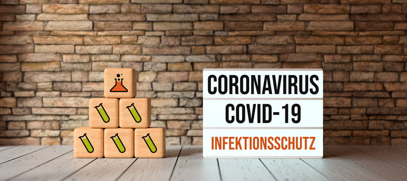 cubes with medical symbols and lightbox with text CORONAVIRUS COVID-19 and INFECTION PROTECTION in German in front of a brick wall