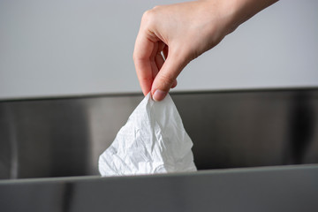 Women hand throwing a white used crumpled tissue paper into a garbage trash bin.
