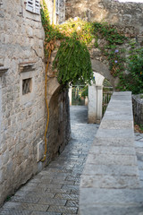 Fragment of an old town street with paved sidewalk, stone walls and an arch