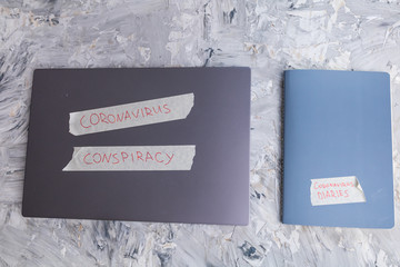 Grey laptop marked Coronavirus conspiracy and notebook Coronavirus diaries on grey background. Illustration of conspiracy theory. Ironic image.  