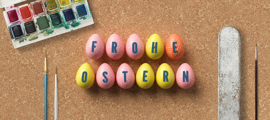 easter eggs with message HAPPY EASTER in German surrounded by brushes and water color boxes on cork background