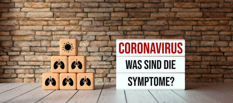 cubes with medical symbols and lightbox with text CORONAVIRUS, WHAT ARE THE SYMPTOMS in German in front of a brick wall