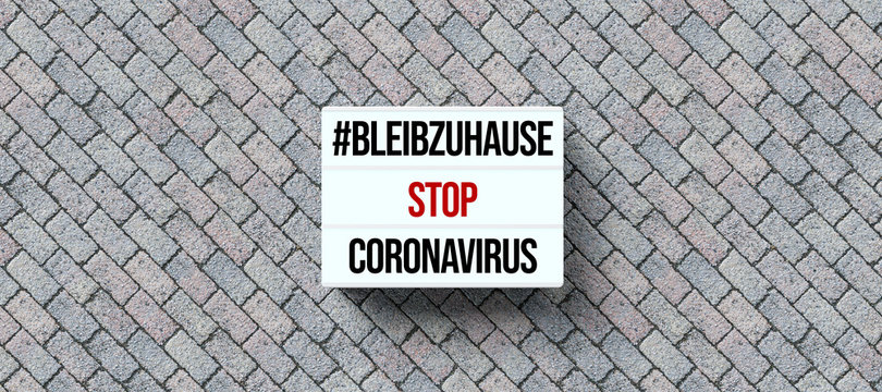 lightbox with text STAY AT HOME, STOP CORONAVIRUS in German on stone pavement