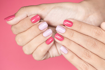 Closeup top view photography of elegant trendy creative bright pink and violet colors manicure. Female hands isolated on pink pastel background.