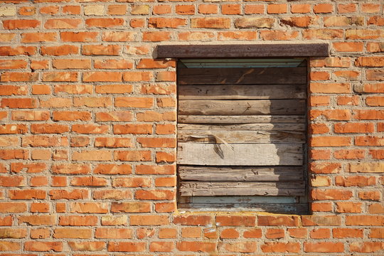 Boarded up with wooden planks window opening in an old red brick wall.