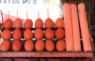 Grilled eggs skewers and khao lam on charcoal stove in the market.