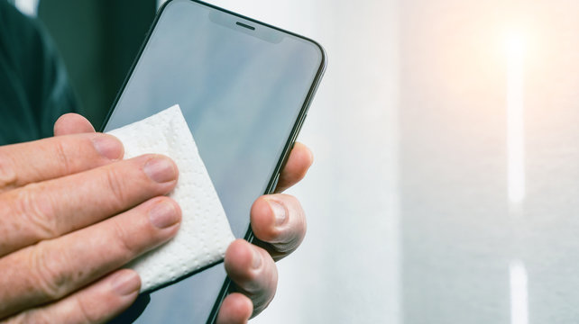 Person Cleaning Mobile Phone Screen With Disinfecting Wipes For Clean Smartphone. COVID-19 Coronavirus Outbreak Contamination Prevention Concept.