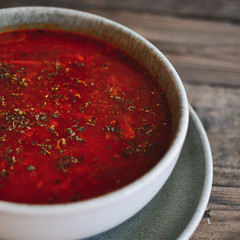 Red borscht in a gray clay bowl. Tomato soup, borsch. Wooden background. Healthy vegetarian and vegan food. Vegetable soup.
