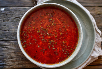 Red borsch in a gray clay bowl. Tomato soup, borscht. Wooden background, top view. Healthy vegetarian and vegan food. Vegetable soup.