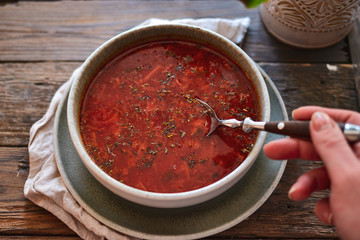 Red borsch in a bowl of gray clay. Tomato soup, borsch. Wooden background Healthy vegetarian and vegan food. Woman holds in hand a bowl and spoon. Food and hands in the frame.